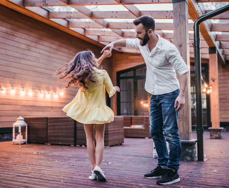 Dad is dancing with his daughter on house's terrace.