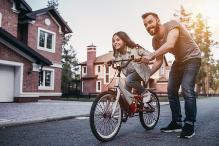 Dad is teaching daughter how to ride bicycle near their private house.の写真素材