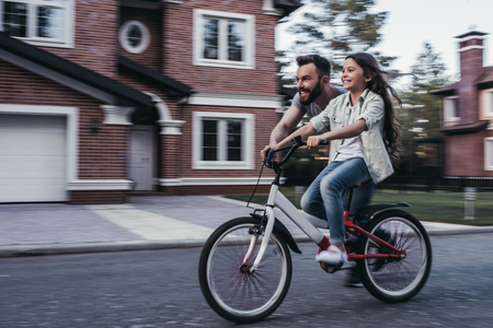 Dad is teaching daughter how to ride bicycle near their private house.の写真素材