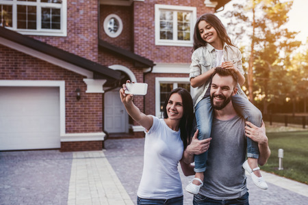 Happy family. Women is taking photo on a smart phone. Modern new house is on the background.