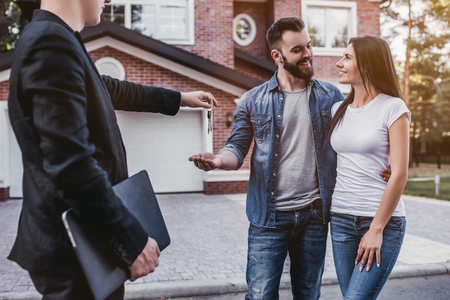 Happy couple is taking keys from their new house from broker. Smiling and looking on each other.の写真素材