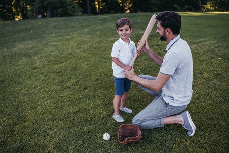 Handsome dad with his little cute sun are playing baseball on green grass lawnの写真素材