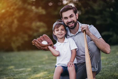 Handsome dad with his little cute sun are playing baseball on green grassy lawnの写真素材