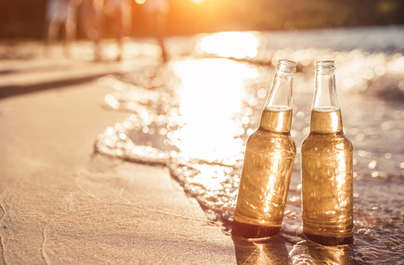 Two bottles of light beer on beach. Sea shore with waves. Group of friends on the background.の写真素材