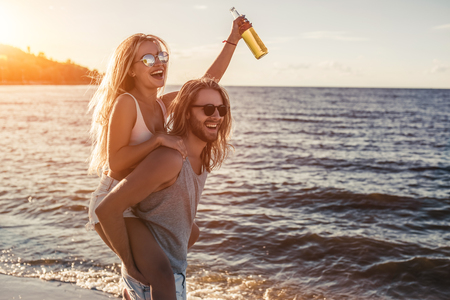 Young beautiful couple is having fun on beach, drinking beach and smiling.の写真素材