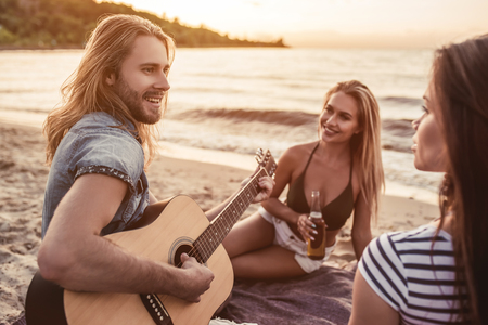 Group of young attractive friends are sitting on beach, playing the guitar and having fun.の写真素材
