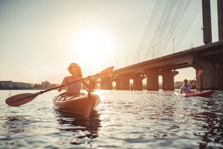 Beautiful young couple is kayaking on river. Waiting for the sunset. Canoeing togetherの写真素材