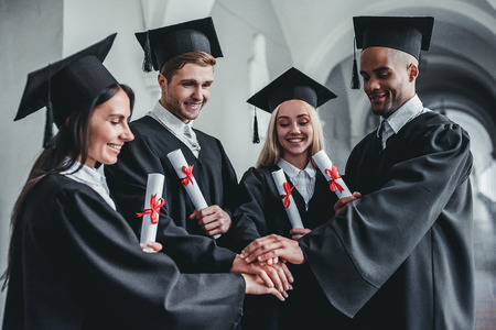 Happy graduates are standing in university hall in mantles with diplomas in hand.の写真素材