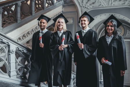 Happy graduates are walking the stairs in university in mantles with diplomas in hand.の写真素材