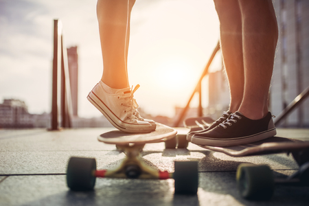 Cropped image of young couple is standing face to face to each other on longboards outdoors. Teenagers with skateboards in the city.の写真素材