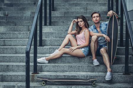 Teenage couple is posing with skateboards in the city. Young man and woman is having fun with longboards.の写真素材