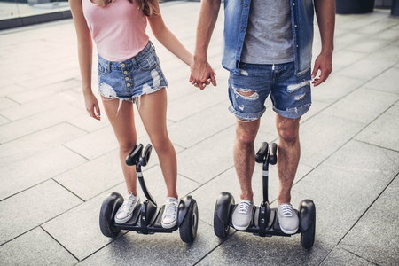 Cropped image of happy teenage couple is having fun in the city. Young man and woman on gyro scooters.の写真素材