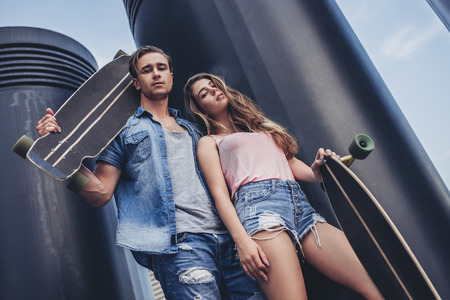 Teenage couple is posing with skateboards in the city. Young man and woman is having fun with longboards.の写真素材