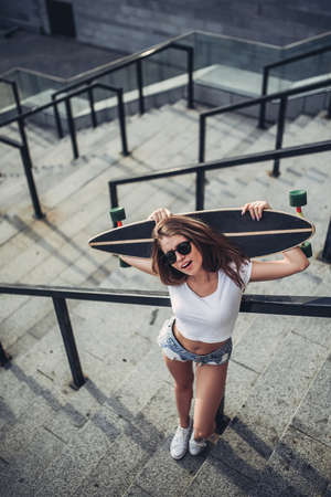 Young woman is posing with skateboard in the city. Female teenager outdoor with longboard.の写真素材