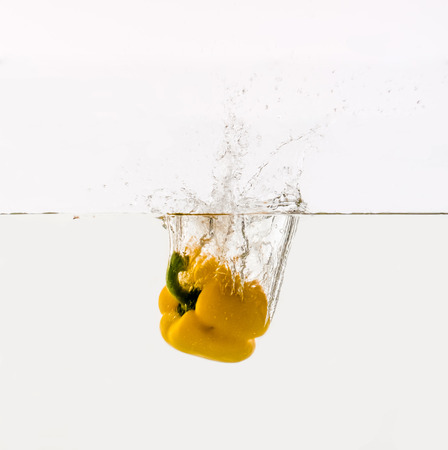 Vegetables are thrown into the water in transparent vessel. Yellow Bulgarian pepper and water splash on white background.の写真素材