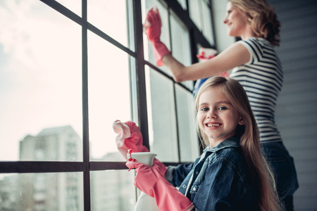 Beautiful young woman  and her little cheerful daughter are doing cleaning at home. Holding cleaning tools and smiling.の写真素材