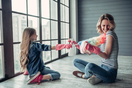 Beautiful young woman  and her little cheerful daughter are having fun while doing cleaning at home. Holding cleaning tools and smiling.の写真素材