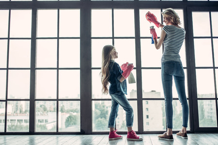 Full-lenght image of beautiful young woman  and her little cheerful daughter are doing cleaning at home.の写真素材