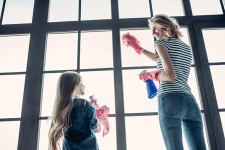 Beautiful young woman  and her little cheerful daughter are doing cleaning at home.の写真素材