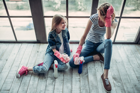 Beautiful young woman  and her little cheerful daughter are doing cleaning at home. Sitting near the cleaning tools and smiling. Good job!の写真素材