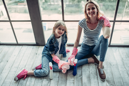 Beautiful young woman  and her little cheerful daughter are doing cleaning at home. Sitting near the cleaning tools and smiling. Good job!の写真素材