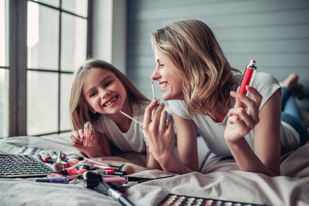 Beautiful mom with her little cute daughter are having fun at home. Doing makeup and smiling.の写真素材