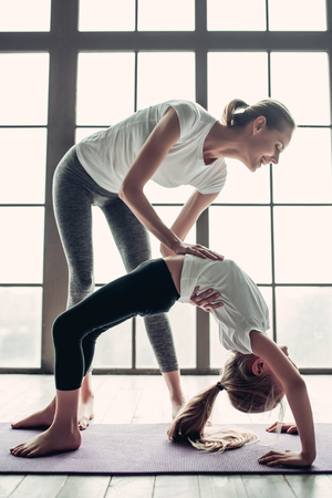 Attractive young mom with her little charming daughter are working out at home. Stretching indoors together. Fitness dayの写真素材