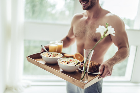 Good morning! Cropped image of handsome sporty man is standing with healthy breakfast in hands.の写真素材