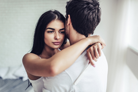 Young couple with pregnancy test. Beautiful pensive woman is hugging her handsome man in bedroom.の写真素材