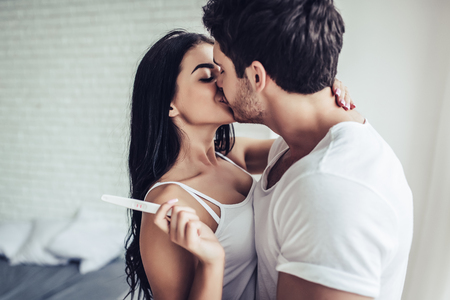I'm pregnant! Happy young couple with pregnancy test is kissing in bedroom.の写真素材