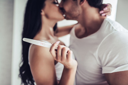 I'm pregnant! Happy young couple with pregnancy test is kissing in bedroom.の写真素材
