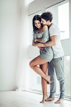 Full-length image of young beautiful couple is enjoying the company of each other at home. Hugging and kissing.の写真素材