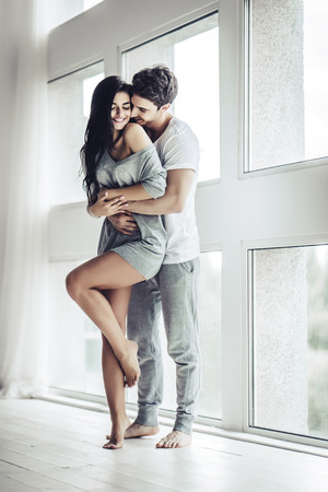 Full-length image of young beautiful couple is enjoying the company of each other at home. Hugging and kissing.の写真素材