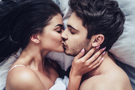 Close-up of happy couple is lying in bed together. Kissing and enjoying the company of each other.の写真素材