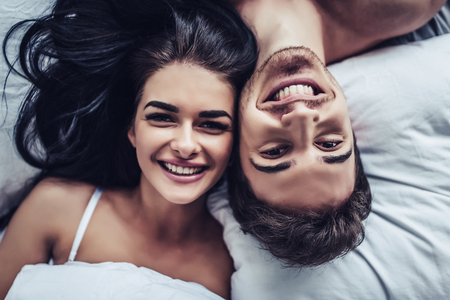 Close-up of happy couple is lying in bed together. Enjoying the company of each other.の写真素材