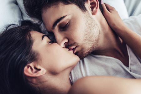 Close-up of happy couple is lying in bed together. Kissing and enjoying the company of each other.の写真素材