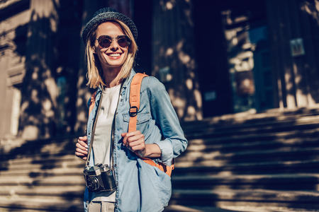 Attractive young female tourist is exploring new city. Woman with retro camera in search of new adventures.の写真素材