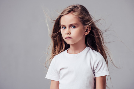 Little cute girl with flying hair isolated. Charming blonde is posing on white background and...