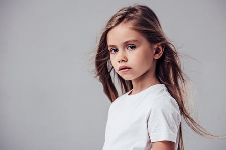 Little cute girl with flying hair isolated. Charming blonde is posing on white background and looking at camera.の写真素材