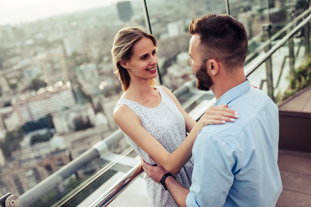 Romantic couple is having fun outside. Enjoying spending time together on a roof terrace with view on city.の写真素材