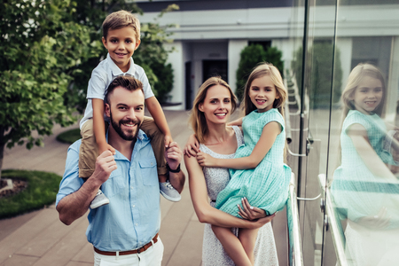 Beautiful family is spending time together  outside. Parents with their children on a roof terrace with view on a city. Mom and dad are having fun with their charming daughter and son.の写真素材