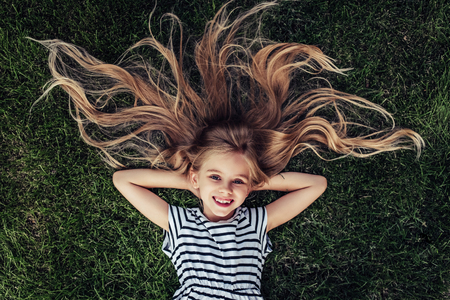 Top view of beautiful little girl is lying on a green grass, smiling and looking at the camera.の写真素材