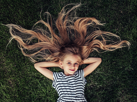 Top view of beautiful little girl is lying on a green grass, smiling and looking at the camera.の写真素材
