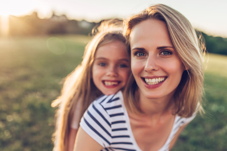Attractive young woman with her little cute daughter are spending time together outdoors. Mom with daughter in park on a green grass during the sunset.の写真素材