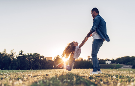 Handsome man is spending time with his little charming daughter outdoors. Dad and daughter are playing in park during the sunset.の写真素材