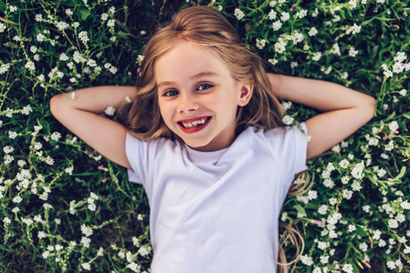 Little charming cute girl is lying on a green floral grass, looking at the camera and smiling.の写真素材