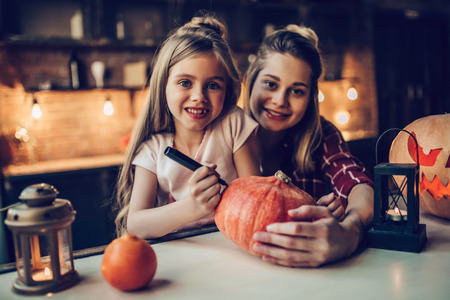 Happy Halloween! Attractive young woman with her little cute daughter are preparing to Halloween on kitchen. Mom with daughter are having fun with pumpkins while painting it.の写真素材