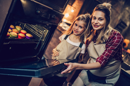 Attractive young pregnant woman with her little cute daughter are cooking cakes on kitchen.の写真素材