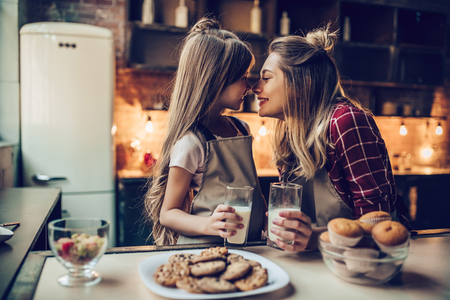 Attractive young woman with her little cute daughter are cooking on kitchen. Drinking milk, eating cakes and cookies.の写真素材