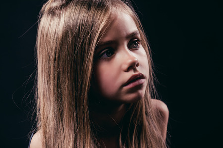 Portrait of little cute girl with long hair is posing on black background. Charming blonde isolated.の写真素材